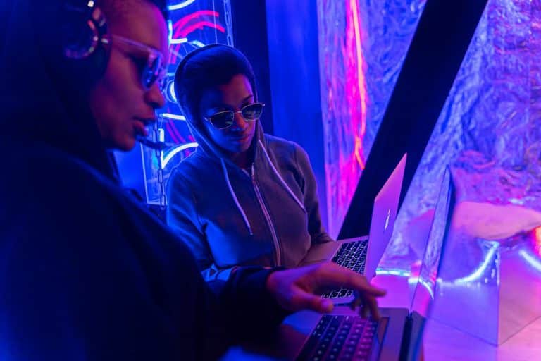 Two individuals working on laptops in a neon-lit setting, emphasizing technology and teamwork.